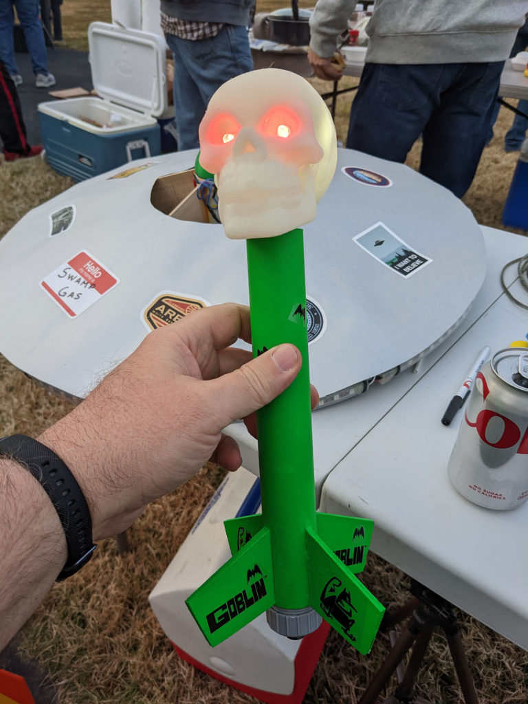 A green Estes "Goblin" model rocket with a skull in place of a nose cone. The skull lights up white, with red eyes.